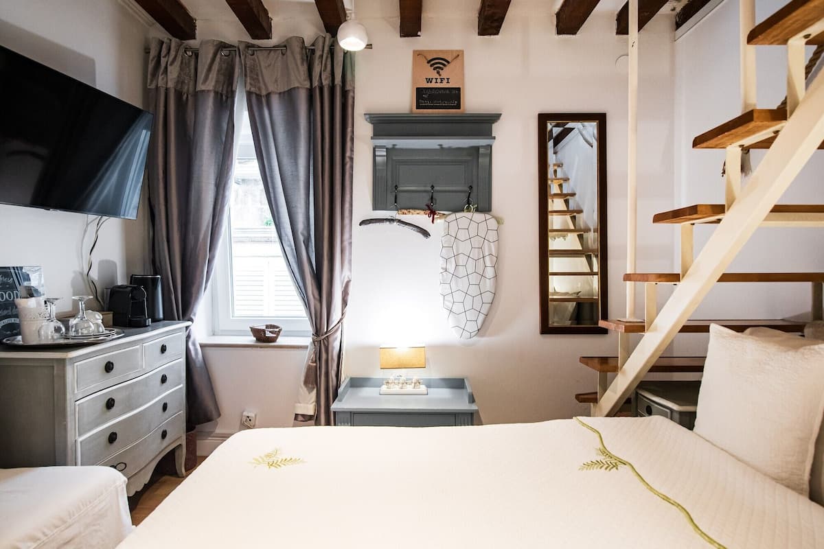 A bedroom with a bed, dresser, TV, and a staircase.