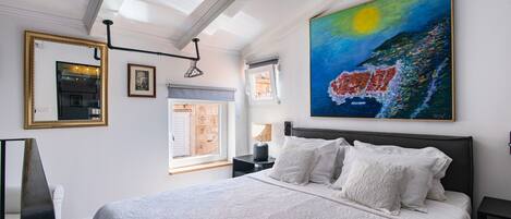 A bedroom with a large bed, a painting of a night scene, and a window with a view of the city.