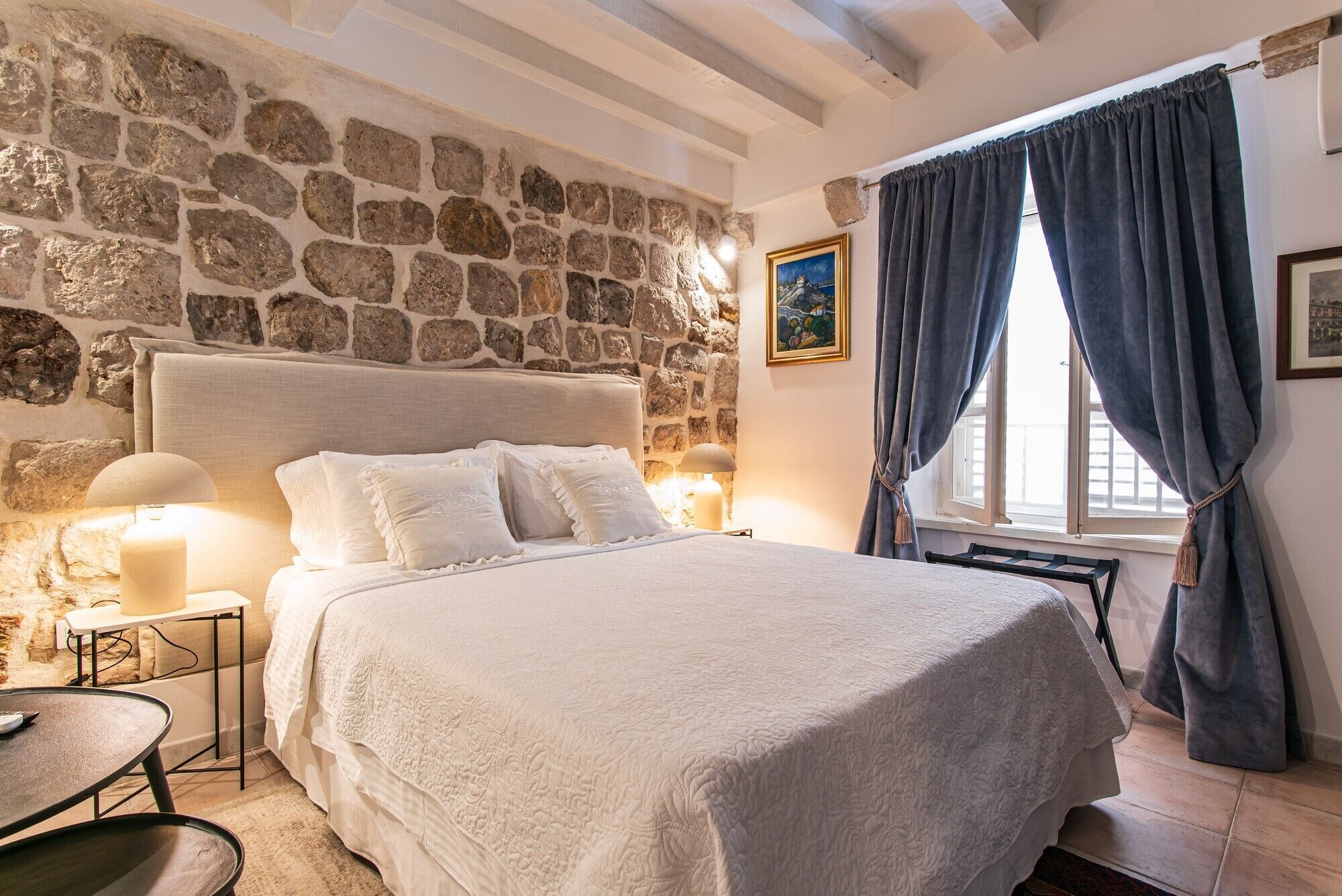 Ein Schlafzimmer mit Stehwand, einem Bett mit weißer Bettwäsche, einem Nachttisch mit Lampe und einem Fenster mit Vorhängen.