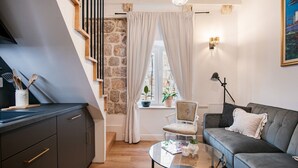 Una sala moderna con un sofá gris, una mesa de centro de vidrio, una pared de piedra y una escalera.