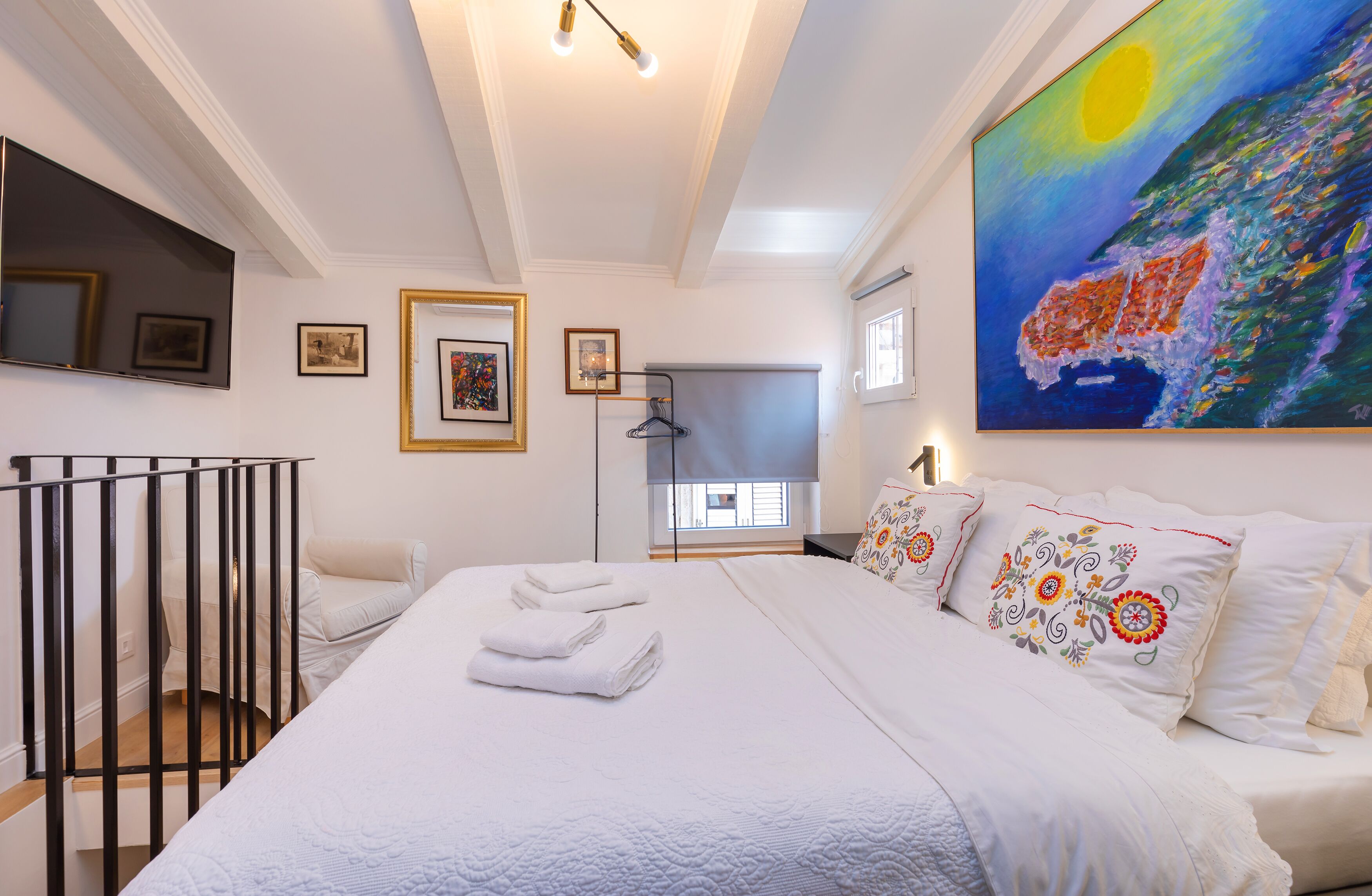 A hotel room with a large bed, a painting on the wall, and a window with blinds.