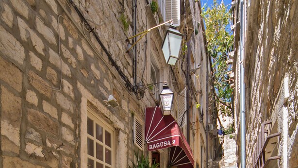 Una estrecha escalera de piedra que sube hacia un edificio con un toldo rojo que dice "RAGUSA 2".