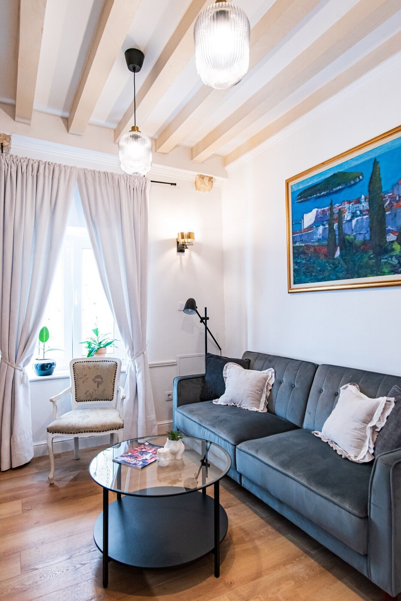A living room with a grey sofa, a round coffee table, a white armchair, and a painting on the wall.