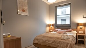 Un dormitorio con cama, lámparas de noche, una ventana y un cuadro en la pared.