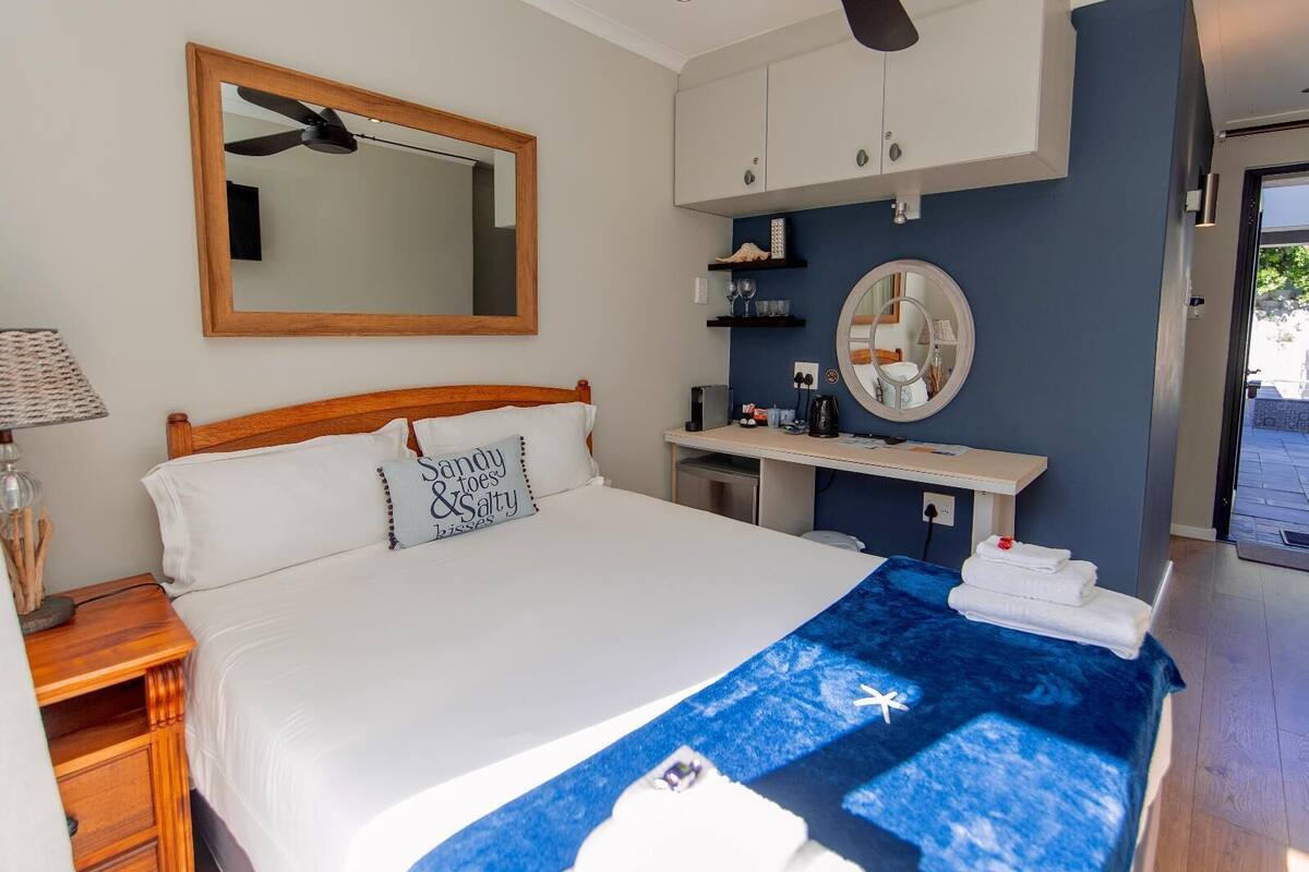 Une chambre à coucher comprenant un lit, un ventilateur de plafond, une table de chevet avec une lampe, une commode, un miroir et une étagère avec des articles de toilette.