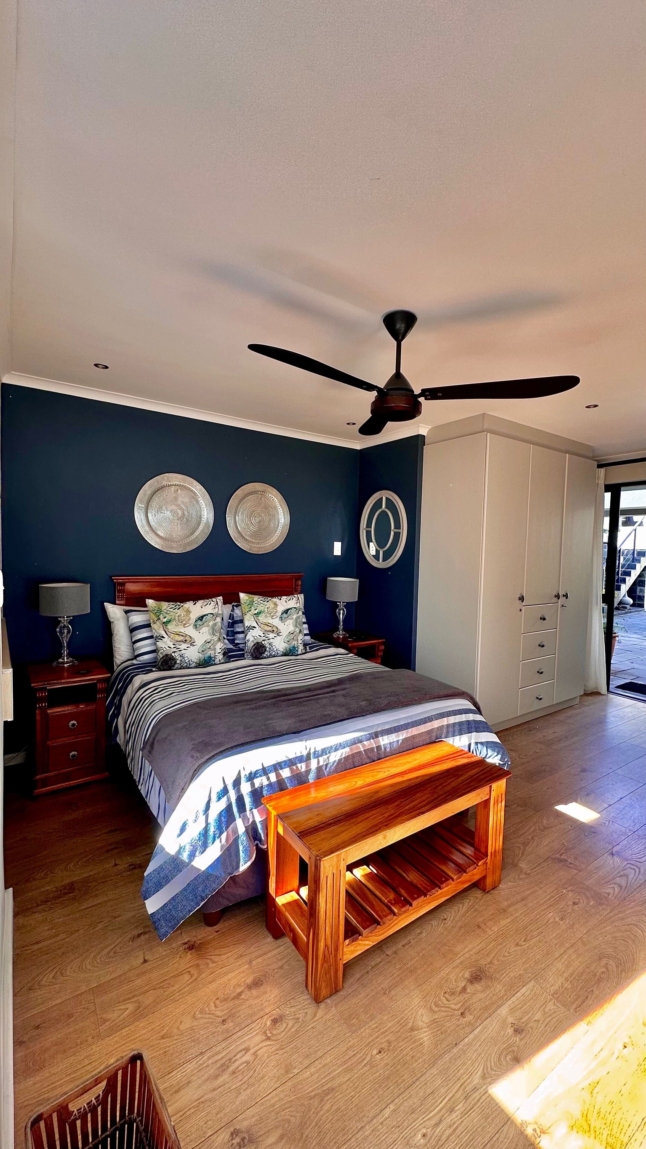 Un dormitorio con cama, ventilador de techo, suelo de madera y vistas al exterior.