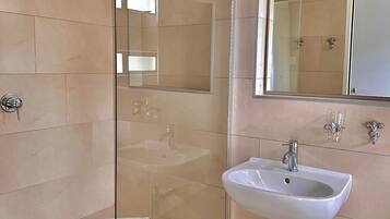 Ein modernes Badezimmer mit einer gläsernen Duschkabine, einem weißen Waschbecken und einem großen Spiegel.