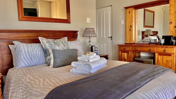 Una cama bien hecha con ropa de cama estampada, una lámpara de noche y un aparador de madera con un espejo.