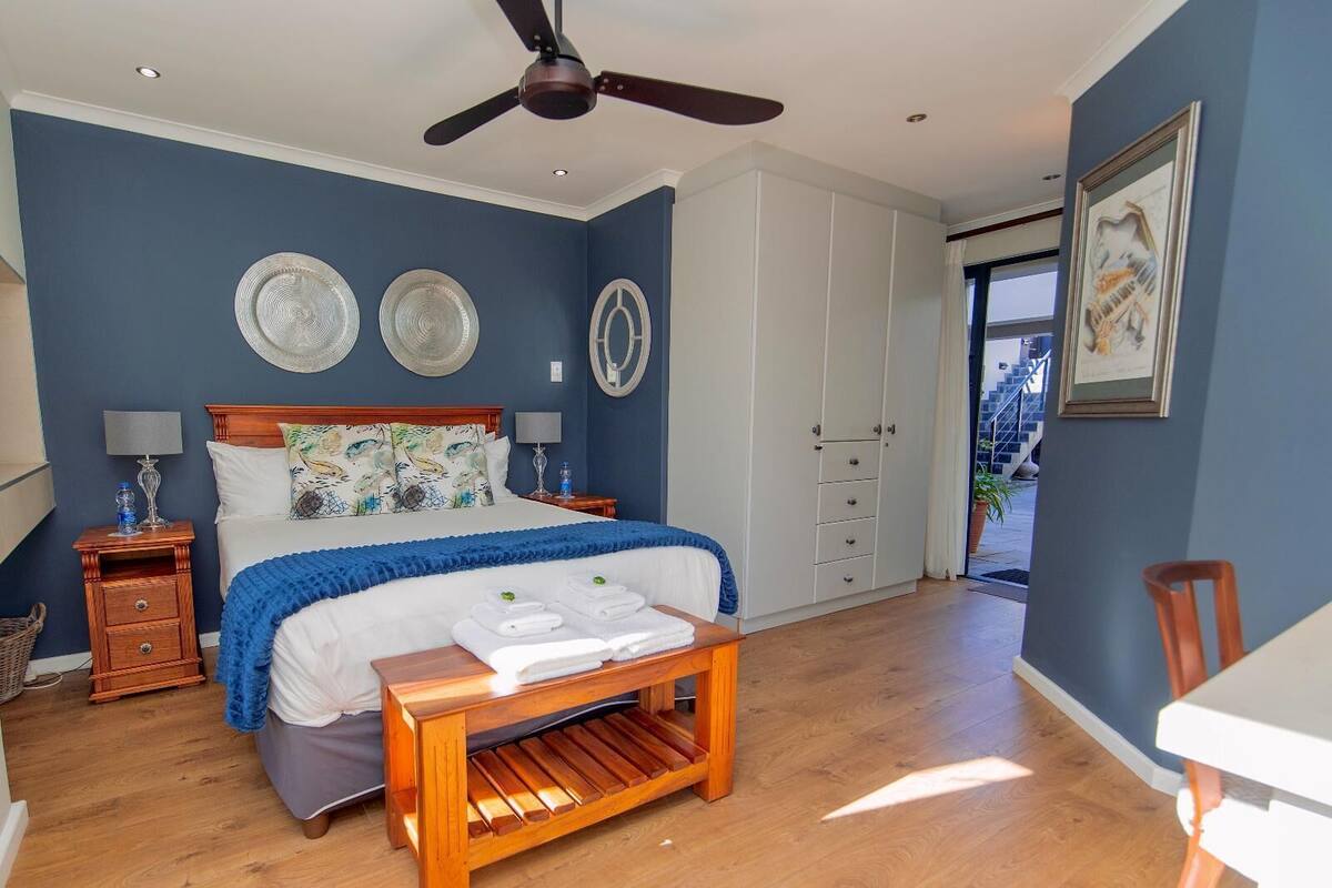 Une chambre à coucher comprenant un lit, des tables de chevet, un banc en bois, un ventilateur de plafond et une armoire.