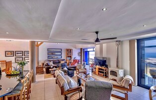 Un salón amplio con un televisor grande, muebles de madera y vistas al océano a través de amplias ventanas.