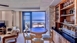 Una cocina moderna con una isla grande, un comedor con una mesa redonda y sillas, y vista al océano a través de un ventanal.