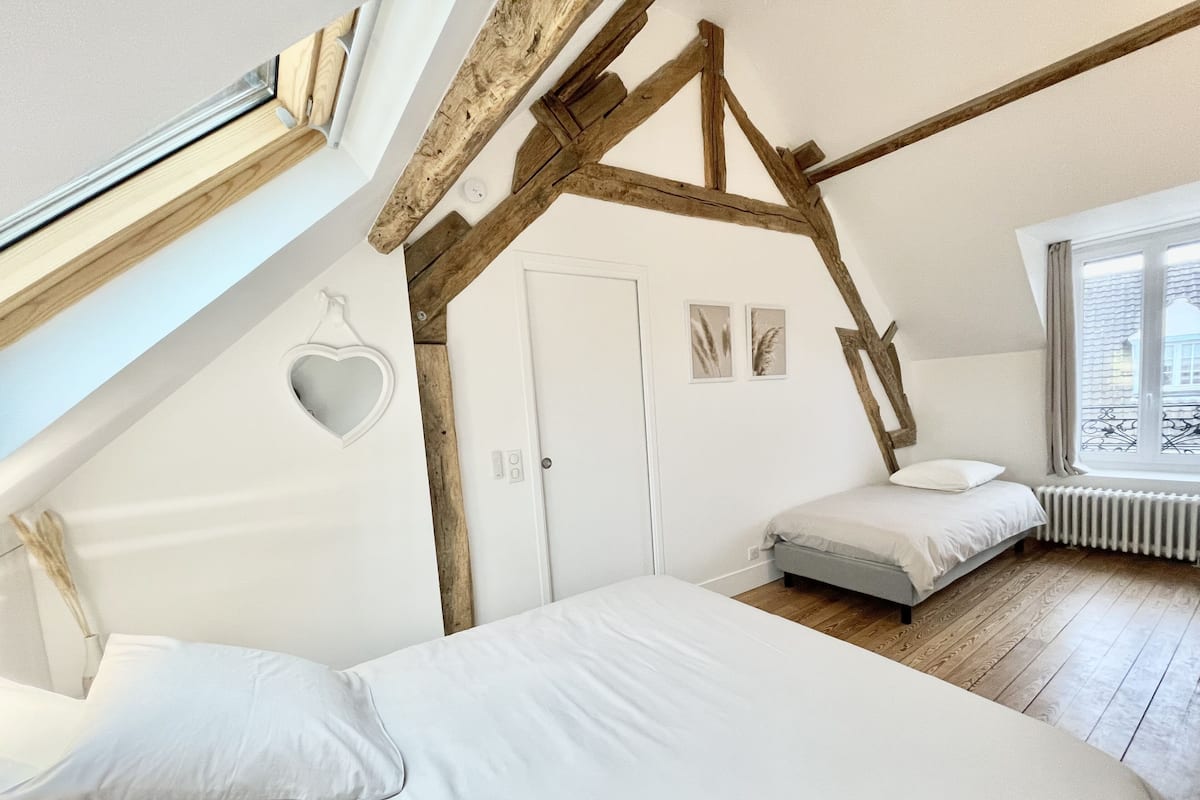 A bedroom with a sloped ceiling, exposed wooden beams, a white door, and a window with a view of the outside.