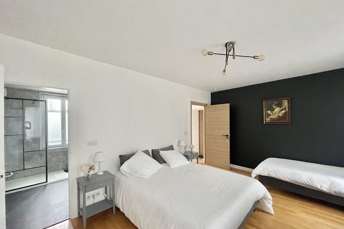 A bedroom with a bed, bedside tables, a nightstand, a mirror, a door, and a painting on the wall.