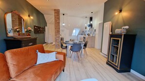 A modern living room with a sofa, dining table, and chairs. There is a kitchen area with a refrigerator and cabinets. - Appartement Tout Neuf, Tout Cocooning et Tout Équipé Pour un Excellent Séjour (Laon)