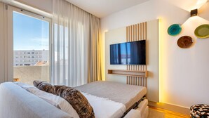 Ein modernes Hotelzimmer mit einem großen Bett, einem an der Wand befestigten Fernseher und einem Balkon mit Blick auf Gebäude.
