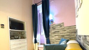 A living room with a yellow sofa, a flat-screen TV on a white cabinet, a wall-mounted air conditioner, and a decorative wall panel. - San Cesareo Apartment (Sorrento)