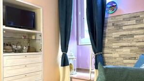 A living room with a TV on a white cabinet, a yellow sofa, and a wooden wall. - San Cesareo Apartment (Sorrento)