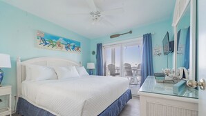 A bedroom with a bed, a ceiling fan, a window with curtains, a chair, and a small table with a mirror.