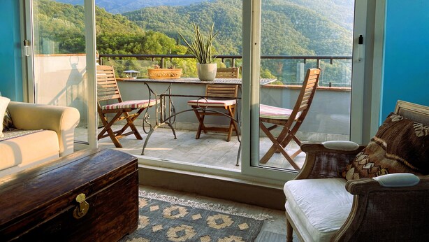 Ein Balkon mit Blick auf grüne Berge, Holzmöbeln und einem Blumentopf.