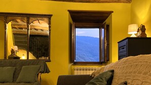 Ein gemütliches Zimmer mit großem Fenster, einem Spiegel und einer Lampe auf einer Kommode.
