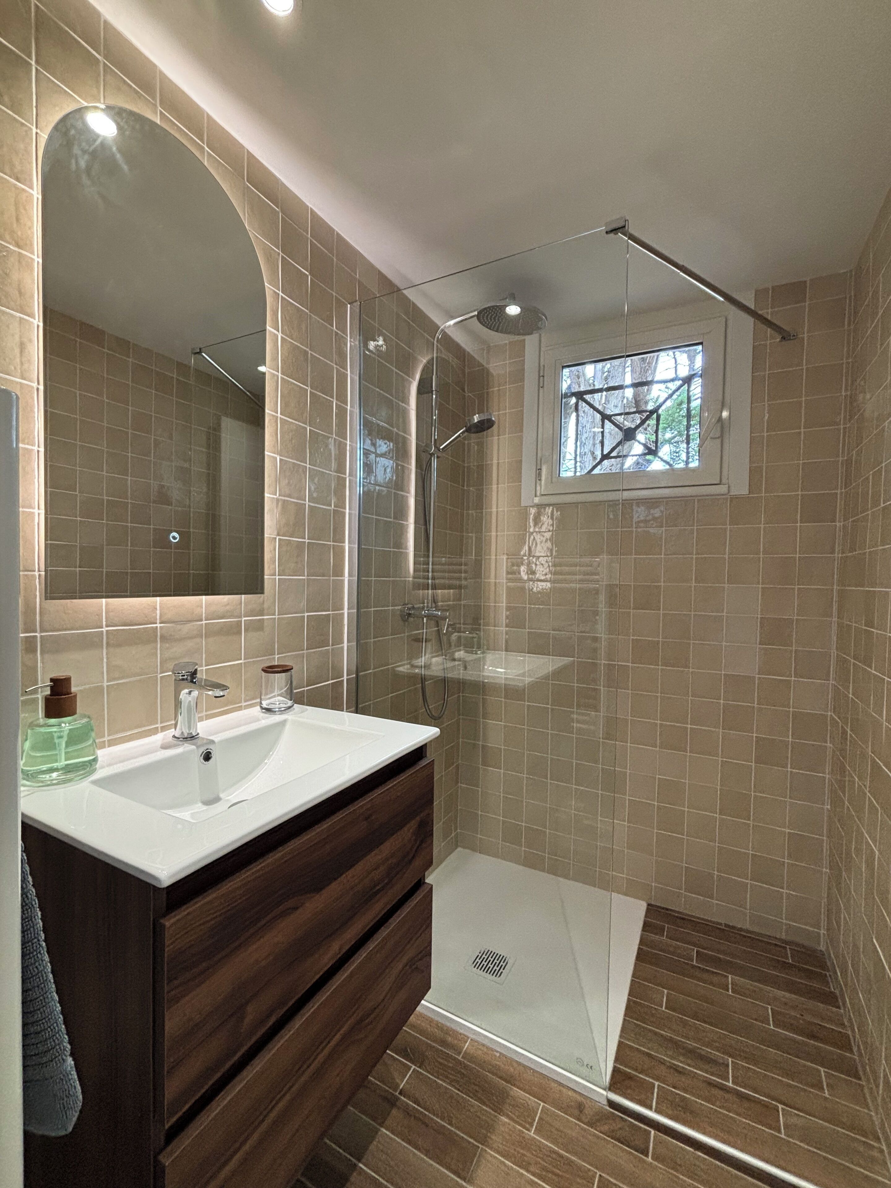 A modern bathroom with a glass-enclosed shower, a large mirror, and a vanity with a sink and storage.