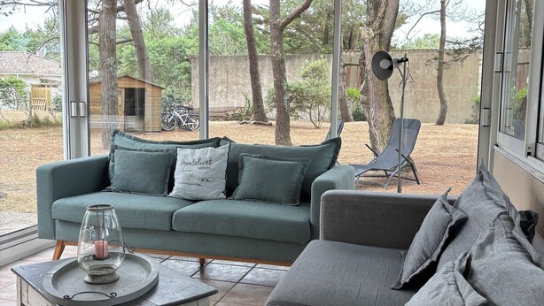 A covered patio with a grey sofa, a green sofa, and a small table with a candle. - Quiet house 200 meters from the ocean (Vendays-Montalivet)
