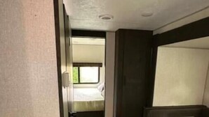 Un corridoio stretto che porta a una camera da letto con finestra, angolo cottura e zona salotto.