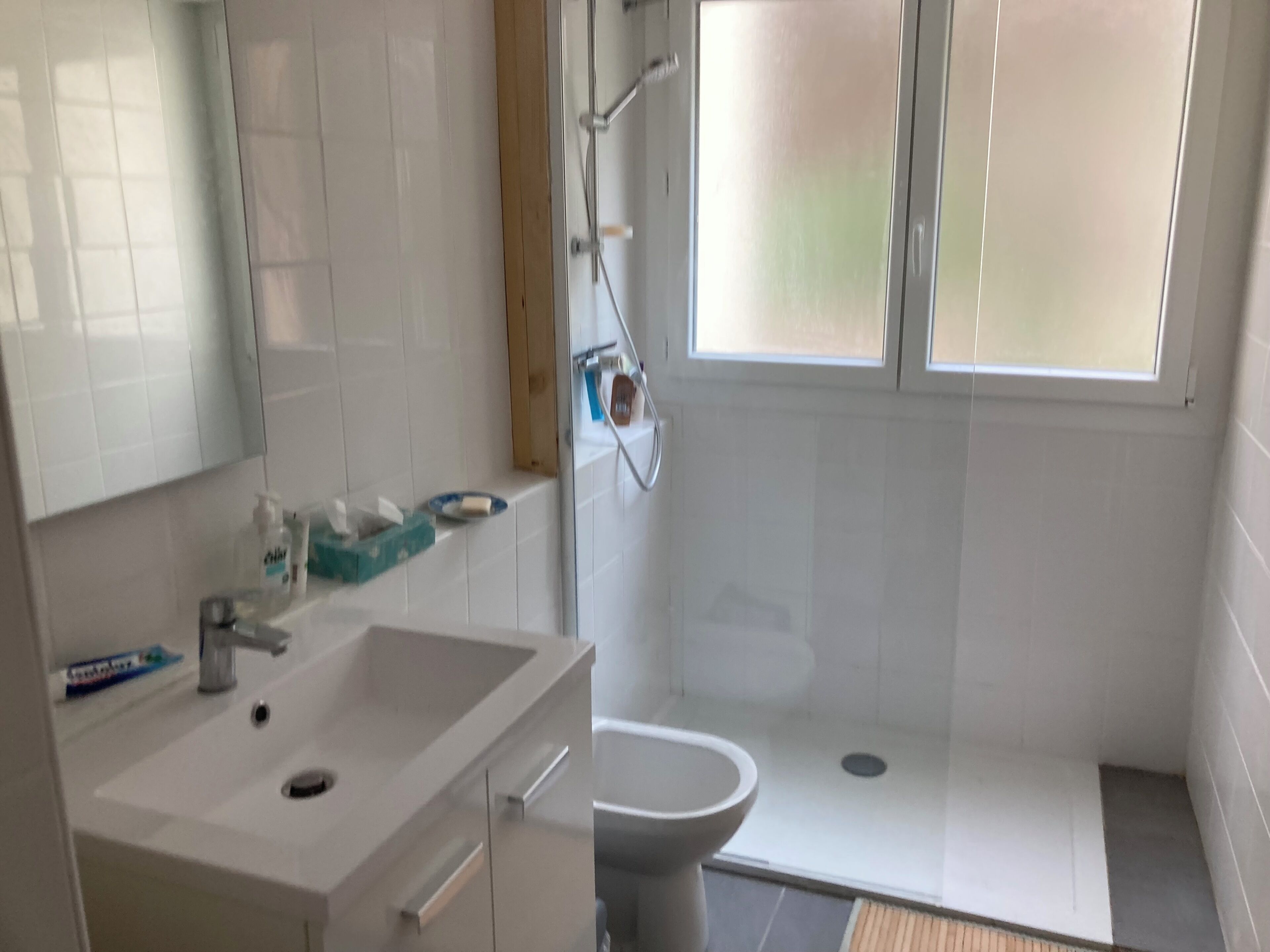 Un baño con lavamanos blanco, espejo y zona de ducha.