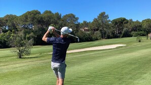 Eine Person spielt Golf auf einem gepflegten Platz mit Bäumen und blauem Himmel.