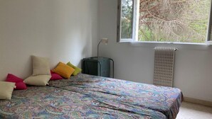 Ein Schlafzimmer mit einem Bett, bunten Kissen, einer Heizung und einem Fenster mit Blick auf Bäume.