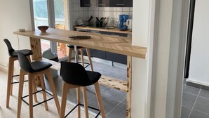 Eine moderne Küche mit einer zentralen Kochinsel, schwarzen Barhocker und Blick auf die Terrasse.