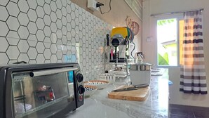 Une cuisine équipée d’un four à micro-ondes, d’une machine à café et d’un grille-pain. Les murs sont recouverts de carreaux et il y a une fenêtre avec des rideaux.