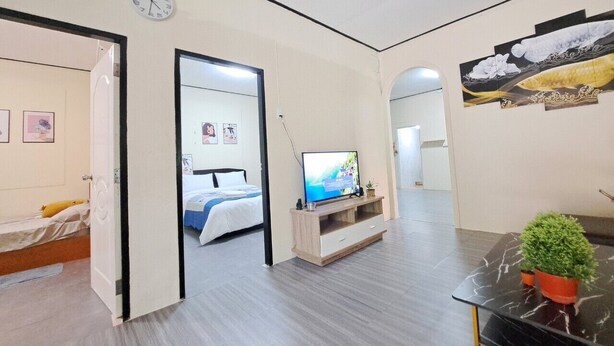 Une chambre d’hôtel moderne équipée d’un lit, d’une télévision, d’une petite table avec une plante et d’une horloge murale.