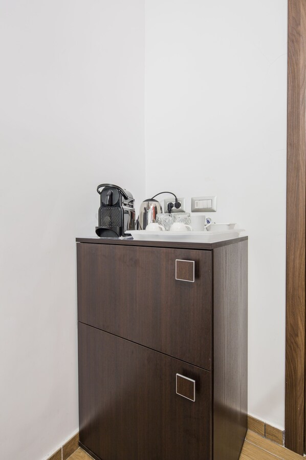 A dark wooden cabinet with two drawers and a countertop with a coffee maker, a kettle, and a mug.