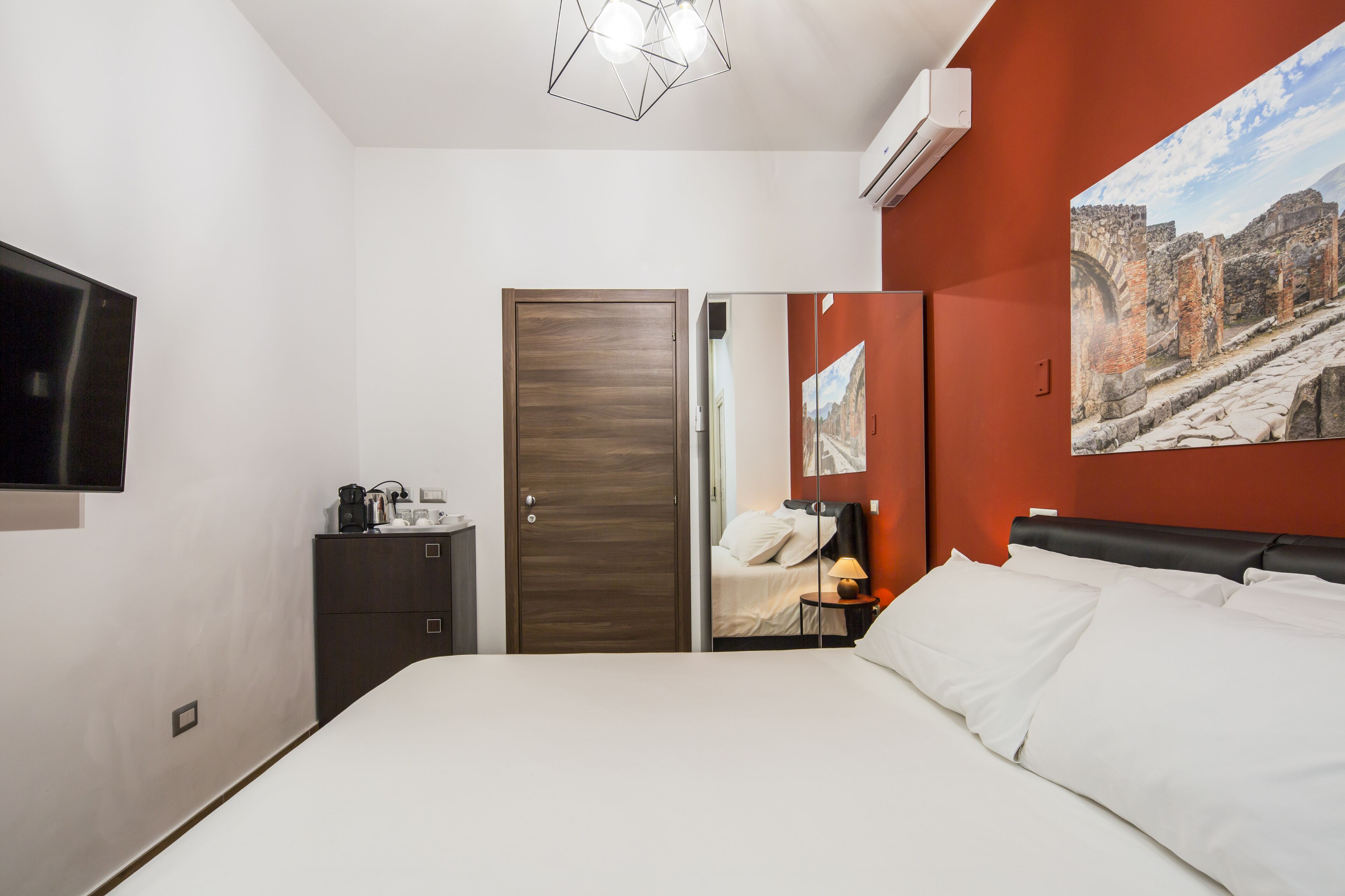 Een hotelkamer met een bed, een kledingkast, een bureau met een lamp en een televisie.