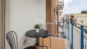 Ein Balkon mit Tisch und Stühlen, einem Blumentopf und Blick auf die Stadtlandschaft.