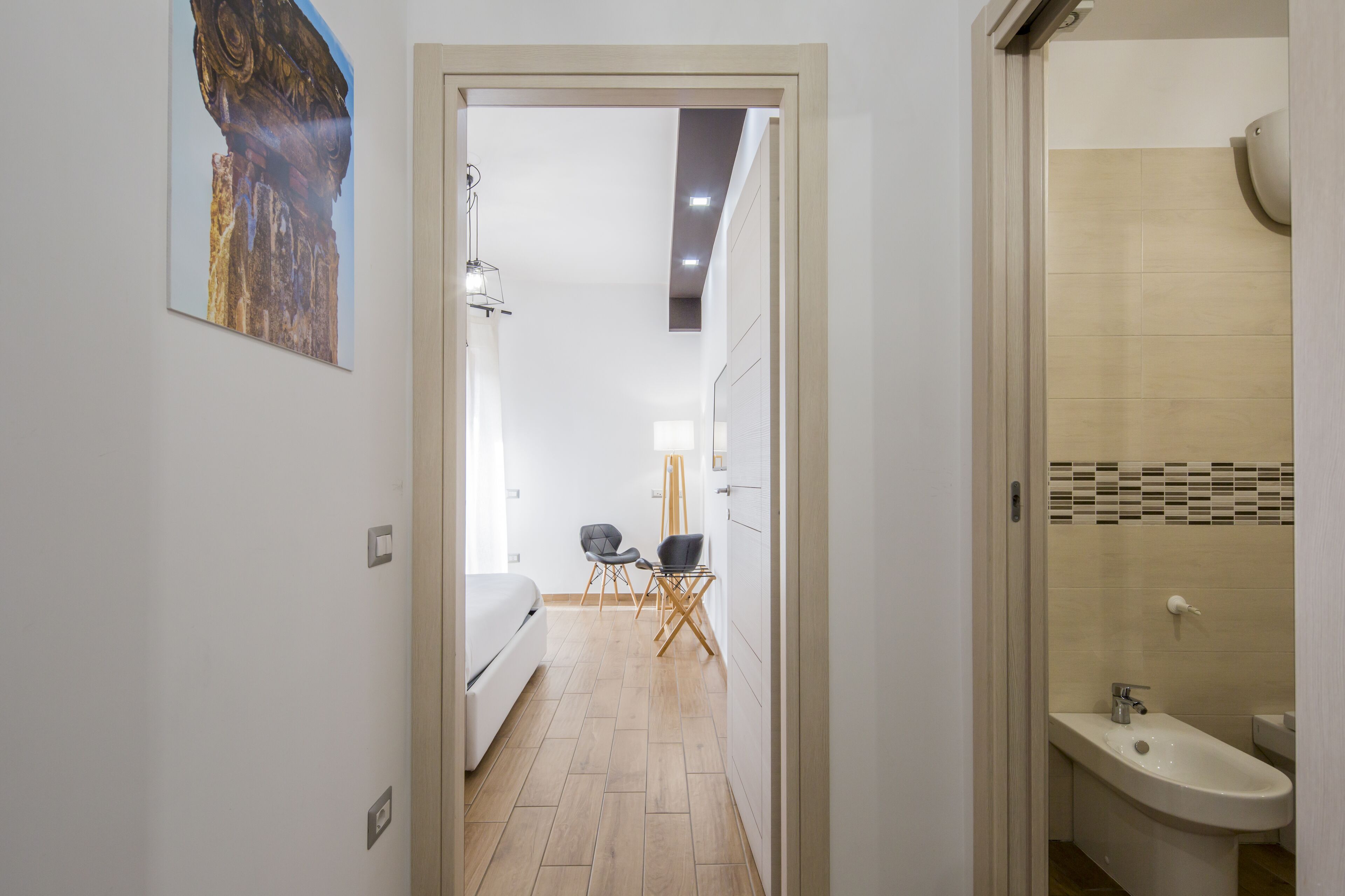 Ein Hotelzimmer mit Bett, Schreibtisch, zwei Stühlen, einer Lampe und einem Badezimmer mit Waschbecken und Dusche.