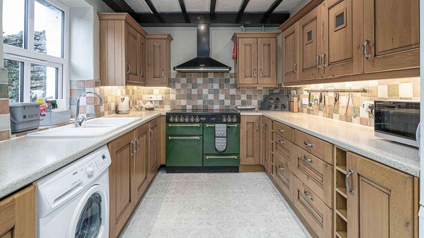 Une cuisine avec des meubles en bois, un poêle vert et un lave-linge.