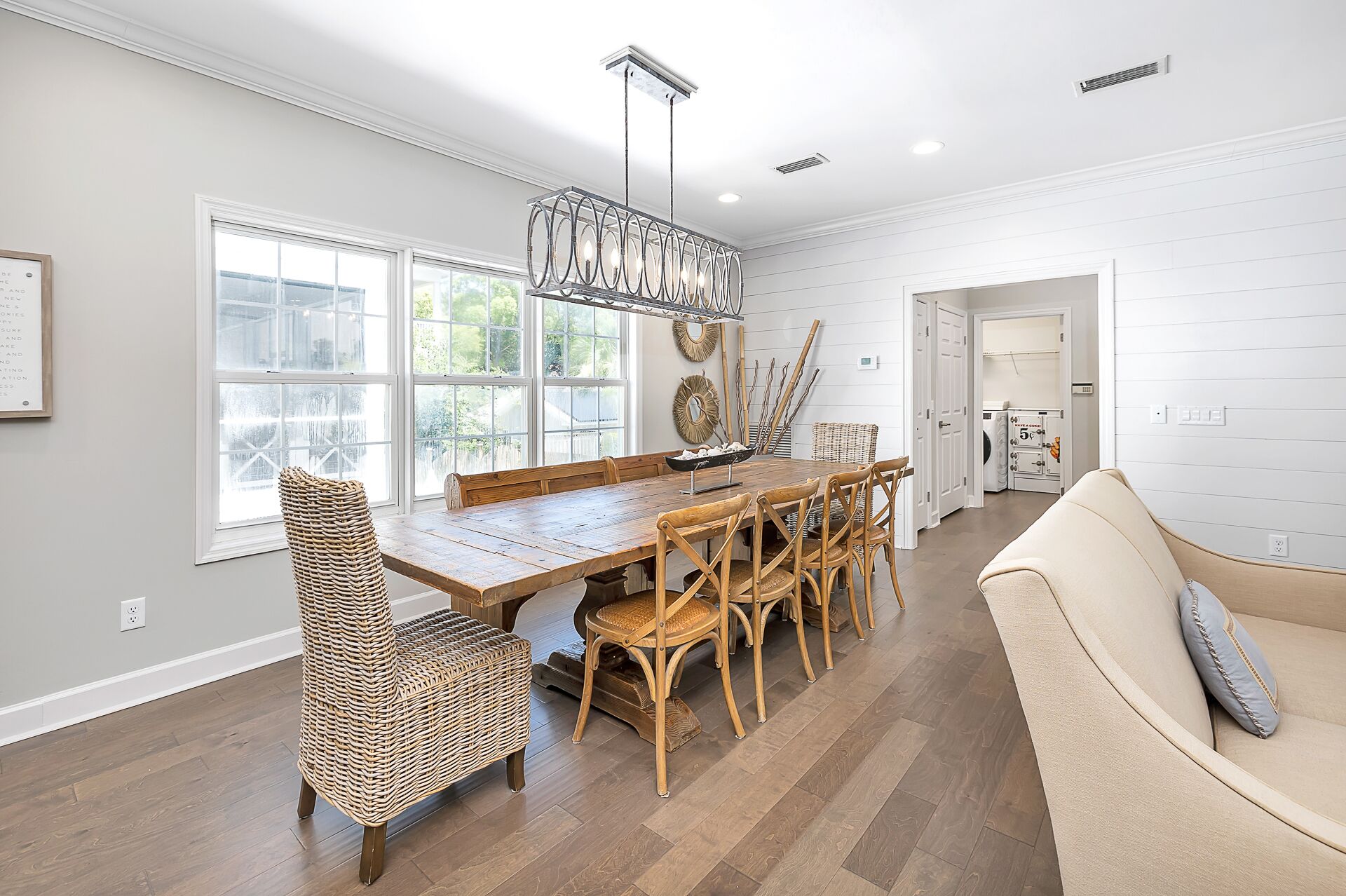 A dining area with a wooden table and chairs, a hanging light fixture, and a view through large windows.