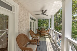 A covered porch with wicker furniture, a ceiling fan, and a view of trees. - Updated Family Home, Steps to Beach, Private Heated Pool (Saint Simons Island)