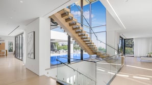 A modern interior with a glass staircase leading to a balcony overlooking a swimming pool.