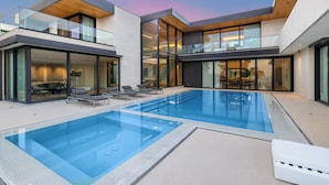 A modern pool area with glass railings, lounge chairs, and a clear blue pool.