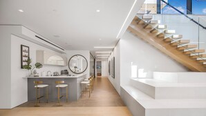 A modern kitchen with bar stools, a central island, and a staircase leading to an upper level.