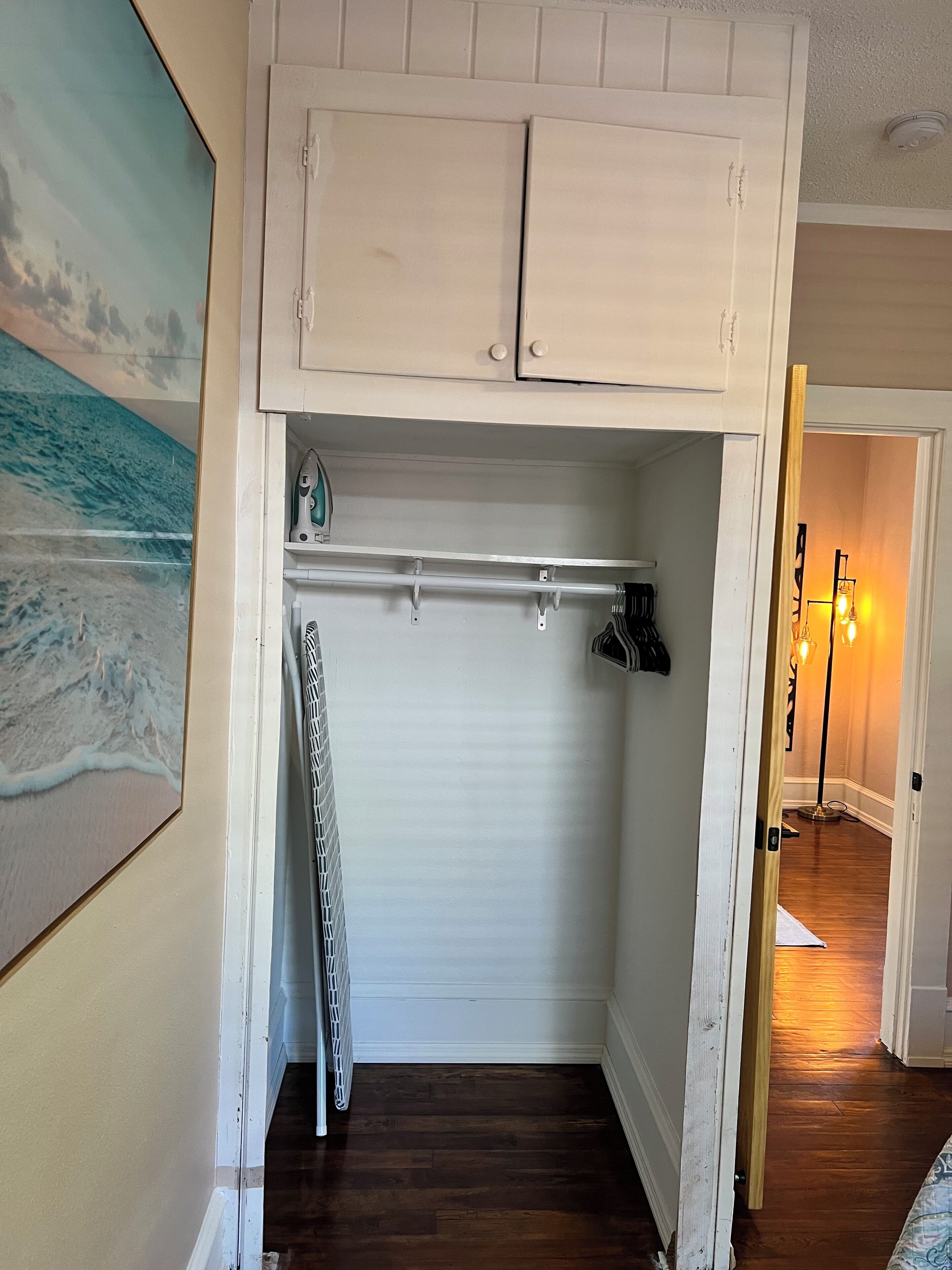 A hallway with a white closet, a wooden floor, and a painting of a beach.