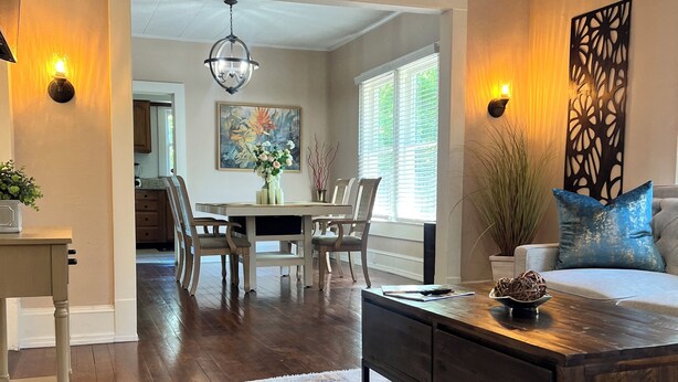 A spacious living room with a dark wooden coffee table, a white sofa with a blue cushion, and a dining area with a white table and chairs. - Relaxing 2-bedroom cottage in beautiful Sanford  (Sanford)