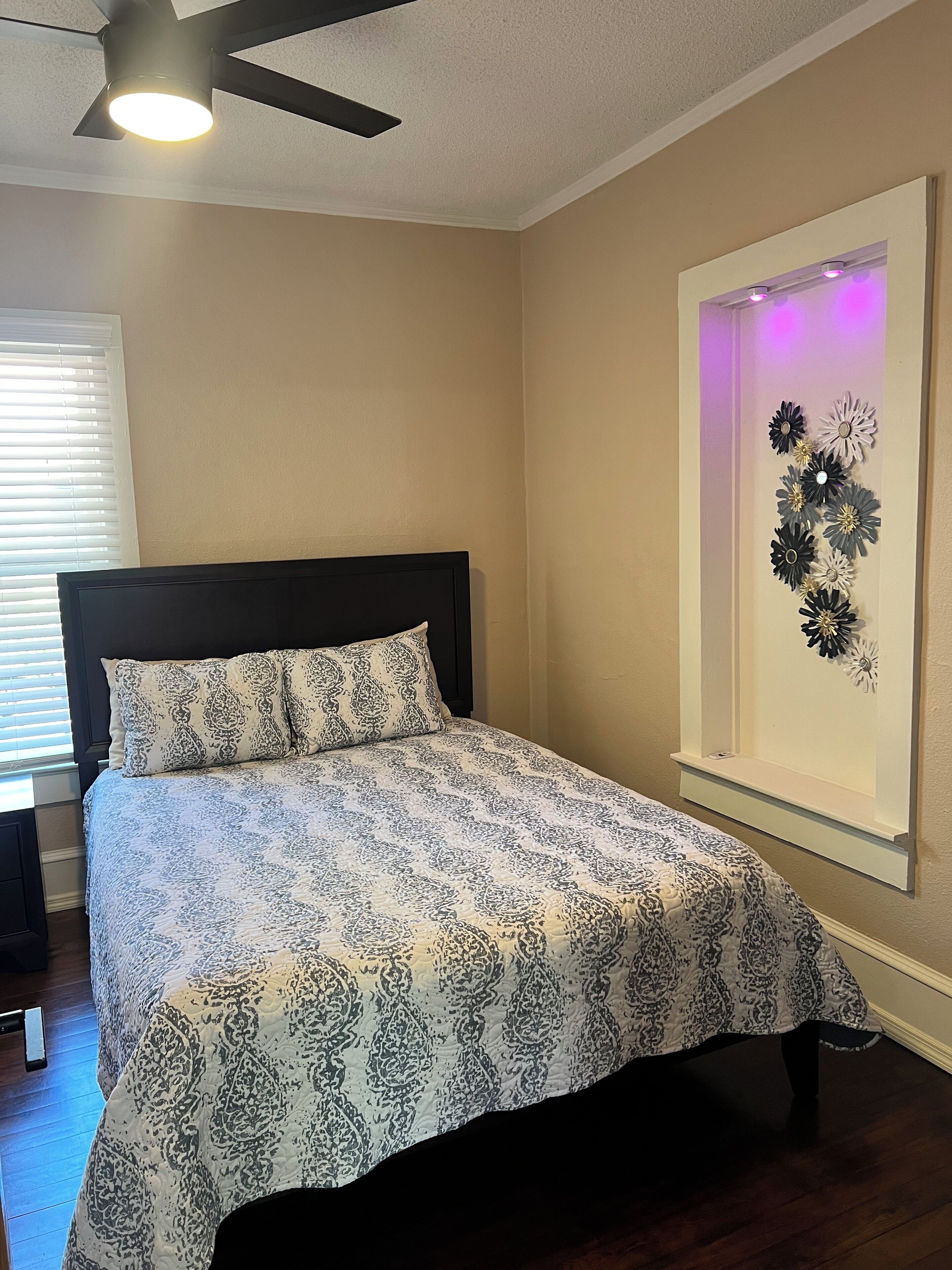 A bedroom with a bed, a ceiling fan, and a wall-mounted light fixture.