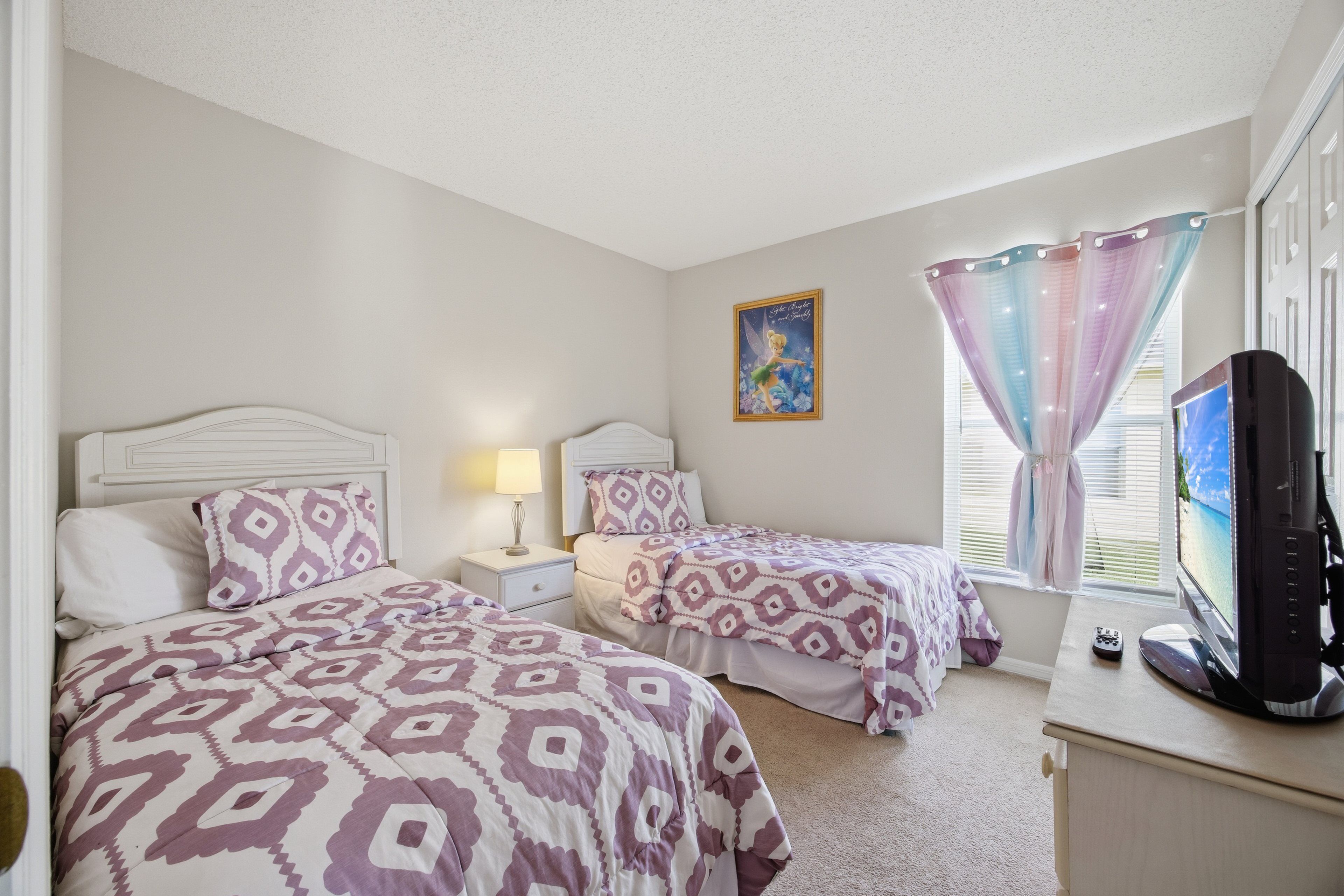 A bedroom with two beds, a television, and a window with curtains.
