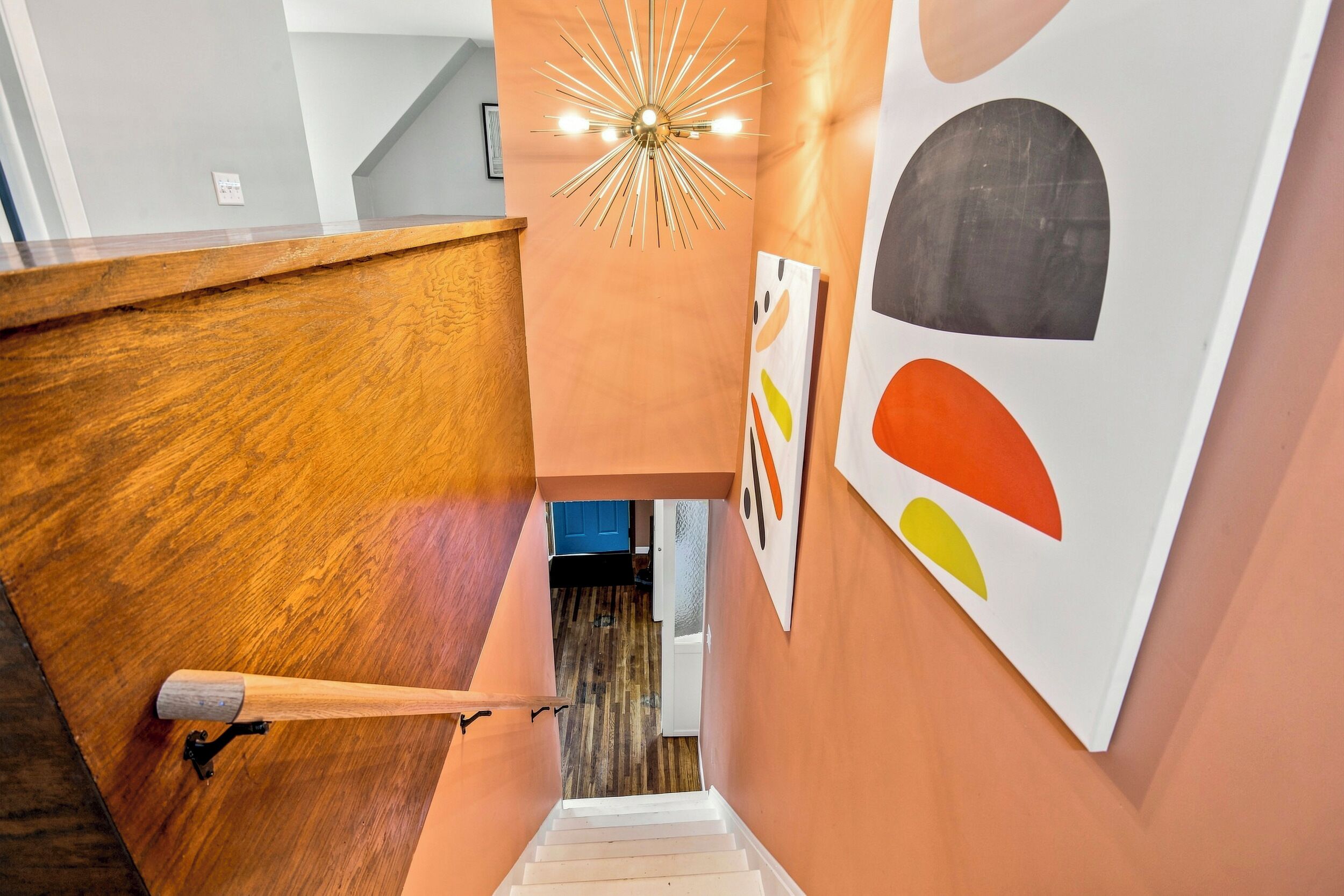 A staircase with a wooden handrail, a modern light fixture, and abstract wall art.