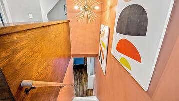 A staircase with a wooden handrail, a modern light fixture, and abstract wall art.
