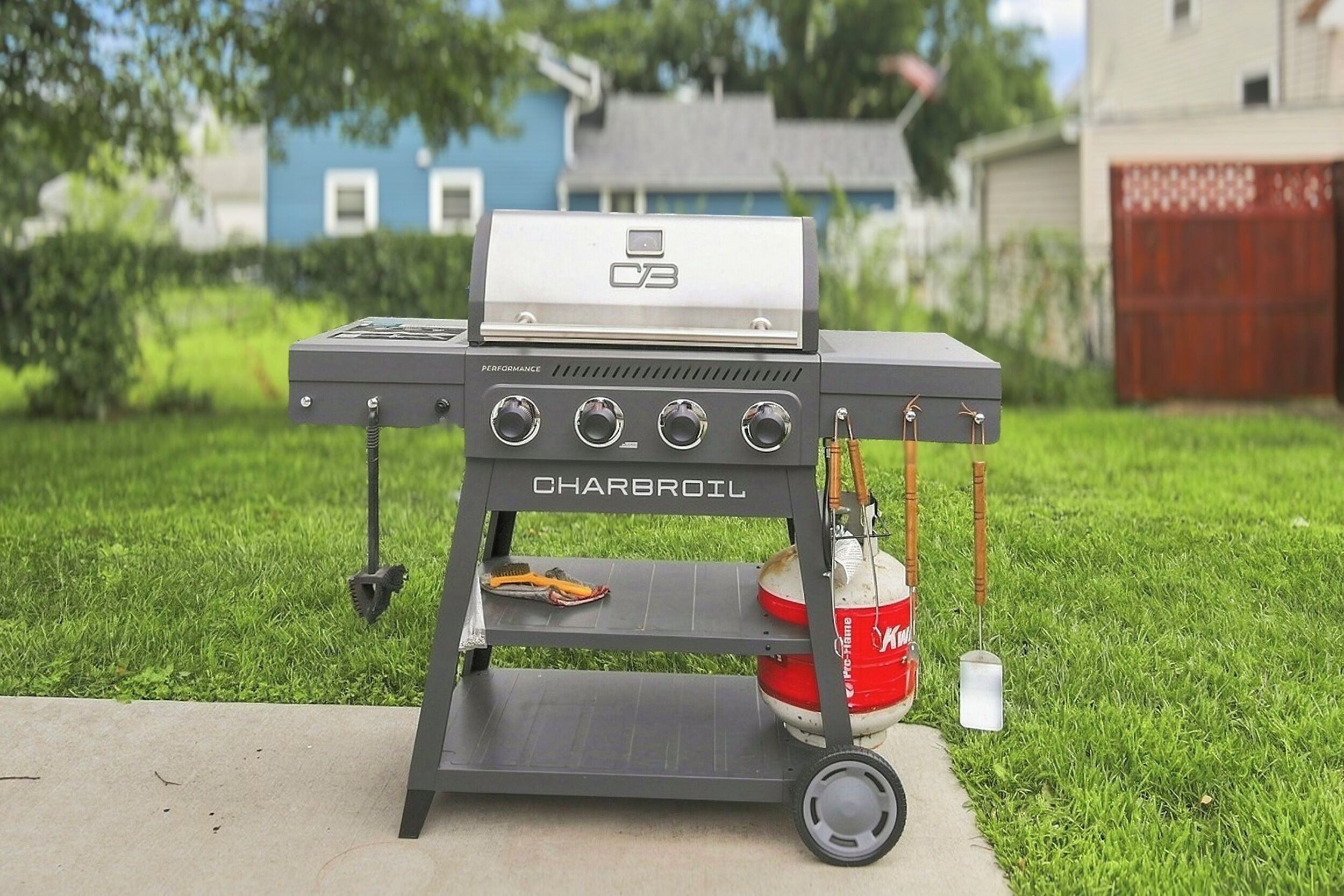 A Charbroil grill with a gas tank, a brush, and a propane tank on a concrete surface.